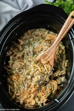 the crock pot is filled with green bean casserole and has a wooden spoon in it