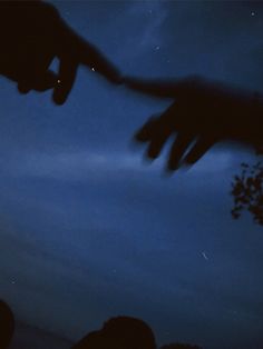 two hands reaching towards each other in the air at night with blue sky and clouds behind them