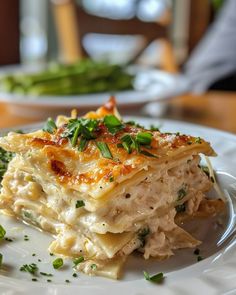 a white plate topped with lasagna covered in cheese and green onions next to asparagus