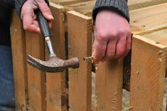 a person holding a hammer and an old tool in their hand while standing next to a wooden fence