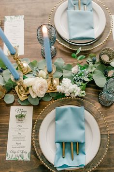 the table is set with blue napkins and gold place settings, candles, and greenery