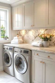 a washer and dryer in a white kitchen with marble counter tops on the counters