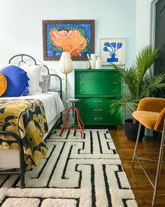 a bed room with a neatly made bed next to a green dresser and two chairs