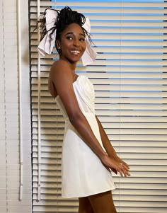 a woman standing in front of a window wearing a white dress and headpiece with one hand on her hip