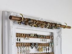 a white frame holds several pairs of earrings and earring hooks on a wall mounted jewelry rack