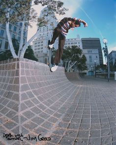 a man riding a skateboard up the side of a brick wall next to a tree