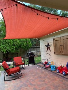 an outdoor patio area with chairs and toys on the brick floor, next to a red awning