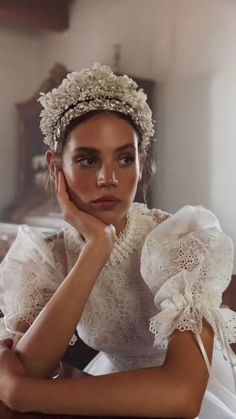 a young woman wearing a white dress and headpiece sitting on a bed with her hands under her chin