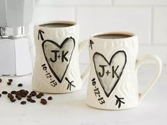 two coffee mugs with hearts and arrows drawn on them next to some coffee beans