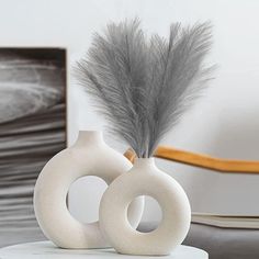 two white vases sitting on top of a table with a feather in the middle