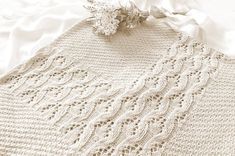 a close up of a knitted blanket on a bed with white sheets and flowers