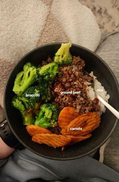 a person holding a pan full of food with broccoli, ground beef and carrots