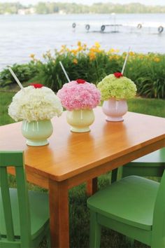 three vases filled with flowers sitting on top of a wooden table next to a lake