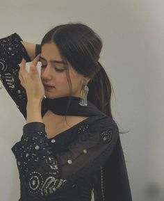 a woman in black dress holding her hand up to her ear and looking down at the ground