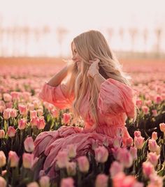 a woman in a pink dress is sitting in a field of tulips with her hands on her head