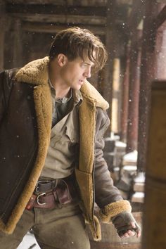 a young man is standing in the snow wearing a brown jacket and holding his hands out