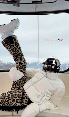 a person in a leopard print coat and ski boots sitting on a boat with their feet up