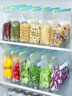 several plastic bags filled with different types of vegetables and fruits in front of an open refrigerator