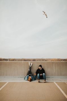 two people sitting on the ground with a bird flying overhead