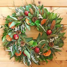 a wreath with apples and greenery is hanging on a wood paneled wall next to a potted plant