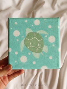 a hand holding up a small painting with a green turtle on it