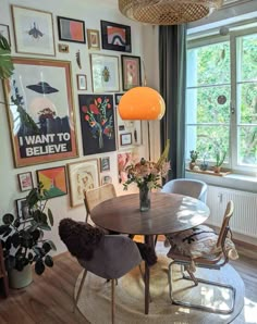 a dining room table surrounded by chairs in front of a window with pictures on the wall