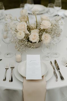 the table is set with white flowers and silverware