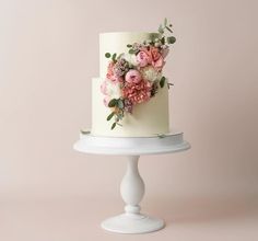 a white cake with flowers on it sitting on top of a table next to a pink wall