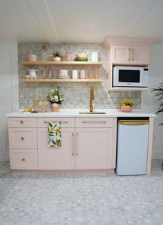 a kitchen with pink cabinets and white counter tops, gold accents on the backsplash