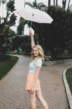 a woman holding an umbrella in the air on a brick walkway with palm trees behind her