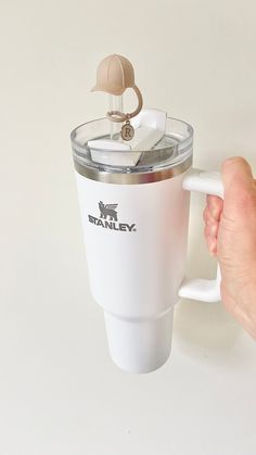 a hand holding a white coffee cup with a ring on the top and handle attached to it