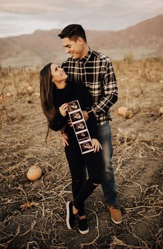 a man and woman standing in the middle of an open field with pumpkins on the ground