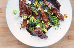 a white plate topped with meat and broccoli covered in sauce on top of a wooden table