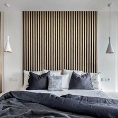 a large bed sitting under two lamps in front of a wooden headboard with vertical stripes on it