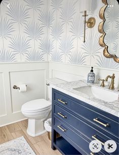 a white toilet sitting next to a sink in a bathroom under a mirror and gold faucet