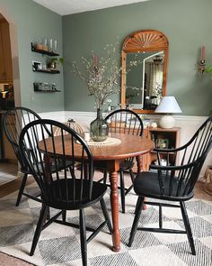 a dining room table with four chairs and a vase on top of it in front of a mirror