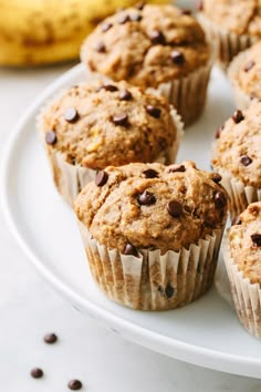 several muffins on a white plate with chocolate chips and bananas in the background