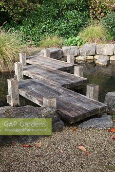 a wooden dock sitting in the middle of a pond surrounded by rocks and grass with a sign that says gap gardens