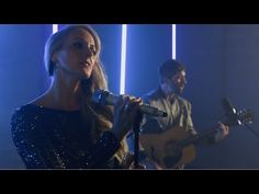 a woman singing into a microphone while standing next to a man holding a guitar in front of her