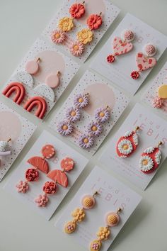 several different types of earrings are displayed on the table with white cards and pink envelopes