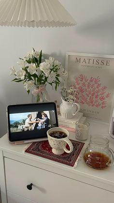 a table topped with a tablet computer next to a cup of coffee and vase filled with flowers