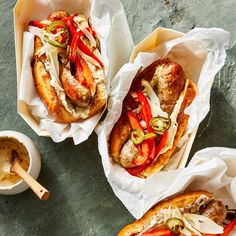 two hot dogs with peppers and onions in buns next to a bowl of dipping sauce