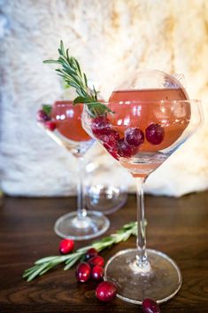 two wine glasses with cranberries and rosemary garnish on the rims