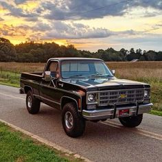 an old pickup truck is parked on the side of the road in front of a field