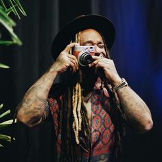 a man with dreadlocks and a hat holding a camera up to his face