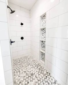 a white tiled shower with black and white tile on the floor, along with shelving unit