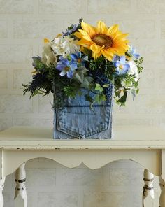 a blue jean vase filled with sunflowers on top of a wooden table next to a white bench