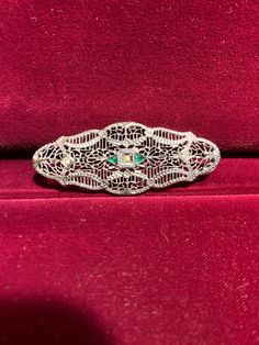 Excellent representation of a classic Victorian Filigree pin in Sterling Silver with white and green synthetic accent stones, which mimic diamond and emerald brooches from that period. This piece from our Estate Collection is in excellent condition. The pin stem is held in place via a safety clasp. This piece may be worn horizontally, vertically, or even on the diagonal, as you wish. It could even be worn vertically on a chain, if desired. While this piece is vintage, it is not technically an antique; although only you need to know as this will easily pass as a well-preserved antique. Elegant Green Diamond Brooch, Green Diamond Wedding Brooches, Vintage Green Diamond Brooches, Elegant Green Oval Brooches, Ornate Diamond Brooches For Formal Occasions, Ornate Diamond Brooch For Formal Wear, Ornate Diamond Brooch For Formal Occasions, Formal Diamond Filigree Brooches, Diamond Filigree Brooches As Gift