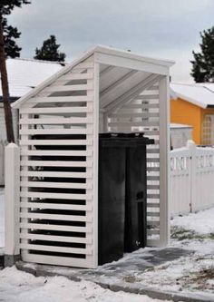 two black trash cans sitting in the snow next to a white fence and yellow house