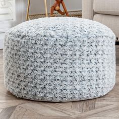 a crocheted ottoman sits on the floor in front of a chair and table